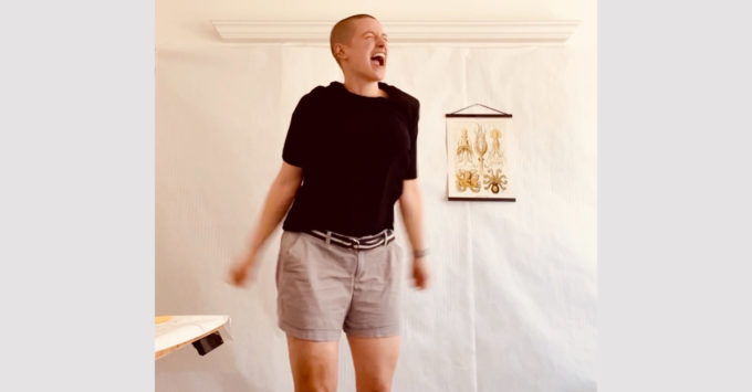 Sarah is caught mid-air while dancing. Her mouth is open in a joyful expression. She is wearing a black t-shirt and khaki shorts.